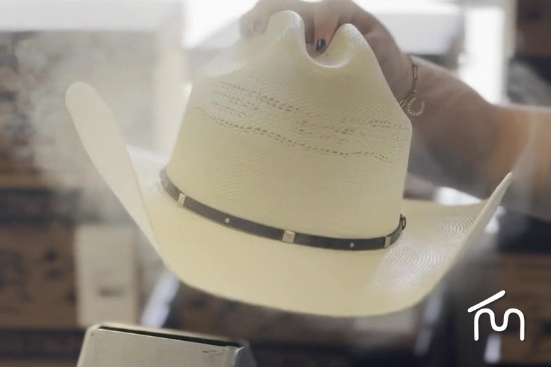 Hands shaping a cream straw cowboy hat crown over the steamer at the Moon Ridge hat bar in Fayetteville
