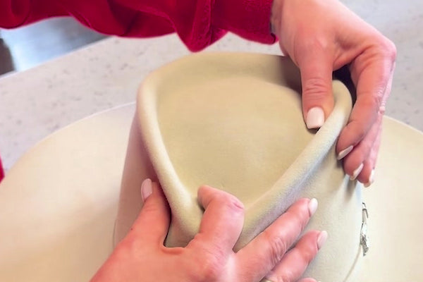 Hands shaping a cream felt cowboy hat crown in the Moon Ridge shop