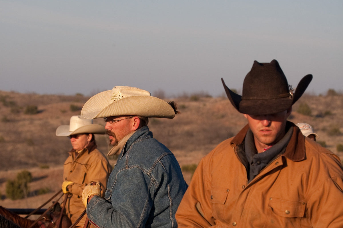 Cowboys in felt and straw hats on the ranch in late-day light