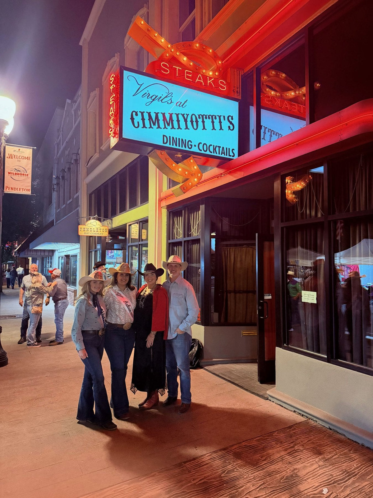 Zack and Natalie with two rodeo queens outside the neon storefront of Virgil's at Cimmiyotti's during Pendleton Round-Up week