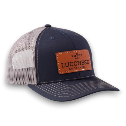 Moon Ridge Hats and Heritage navy and charcoal trucker cap with a brown leather Lucchese Bootmaker logo patch